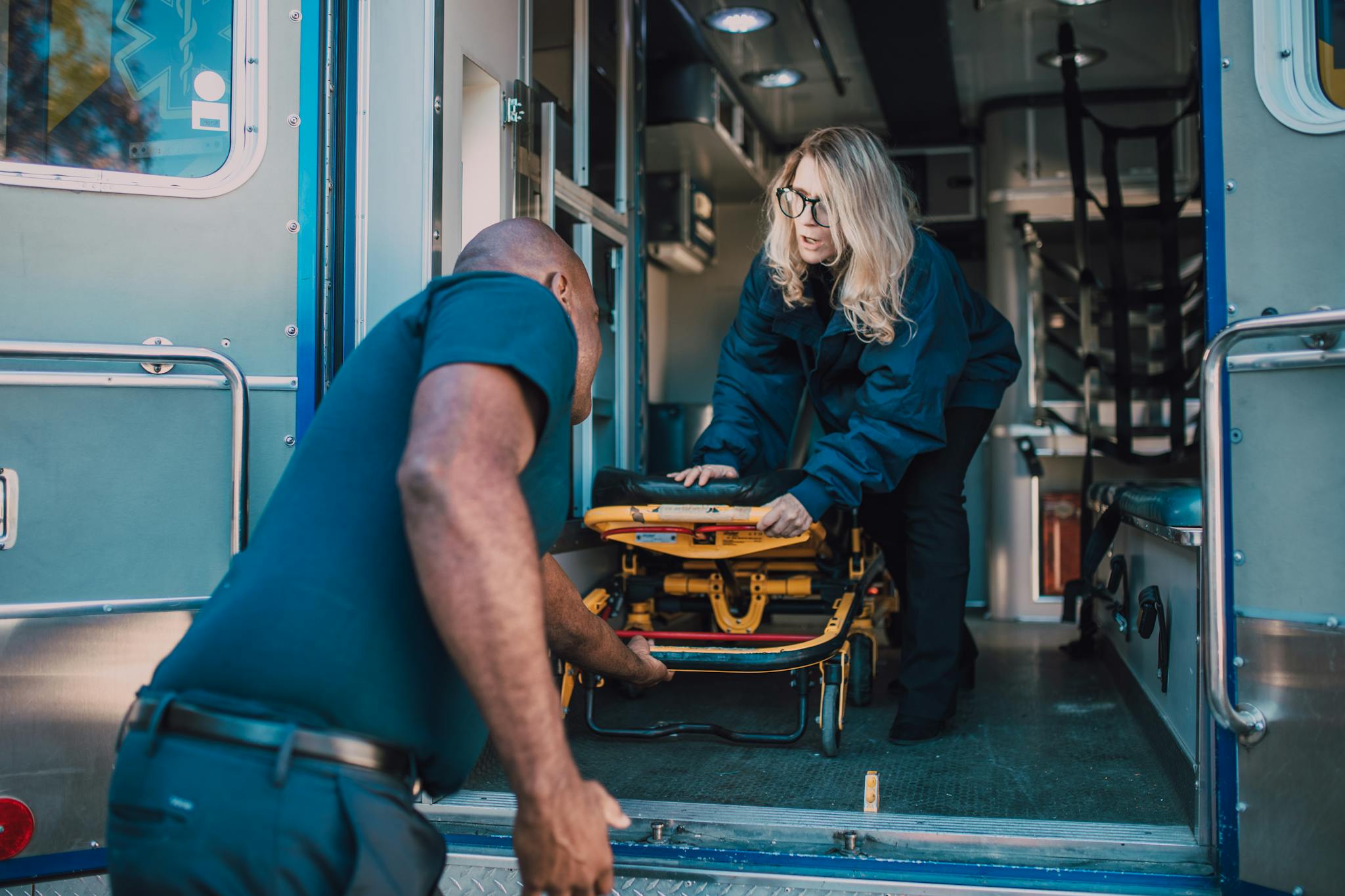 Two paramedics load a stretcher into an ambulance, preparing for emergency transport.